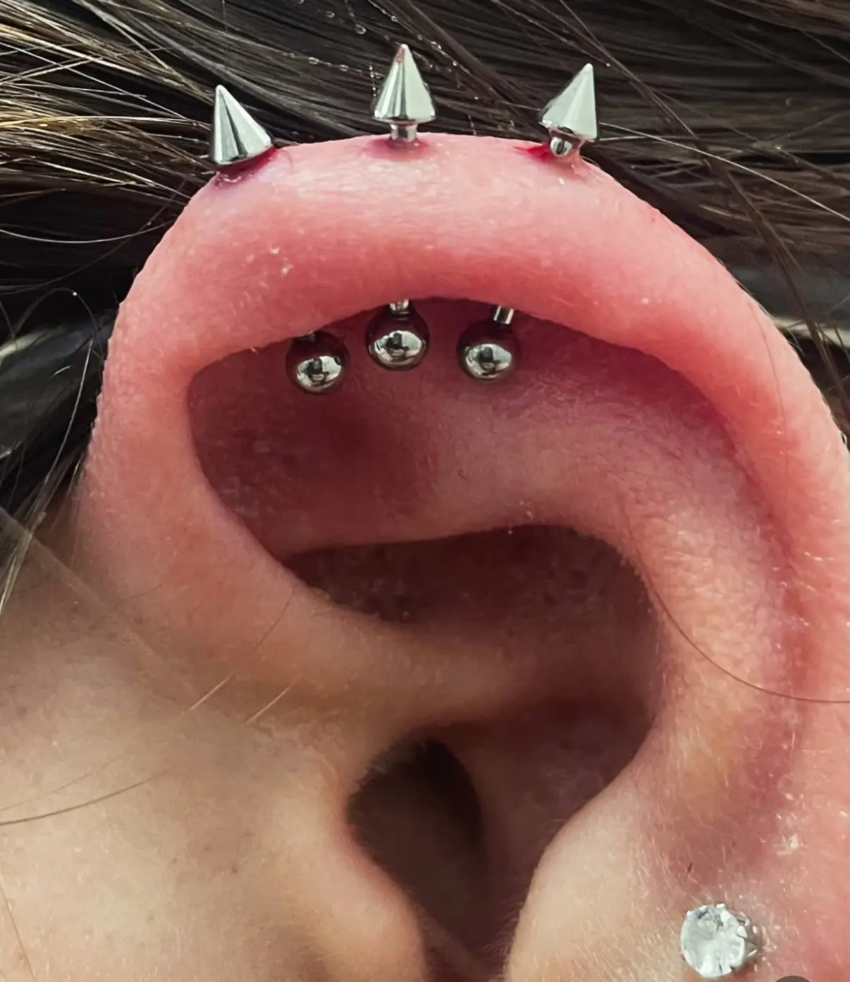 A woman 's ear with three different piercings on it.