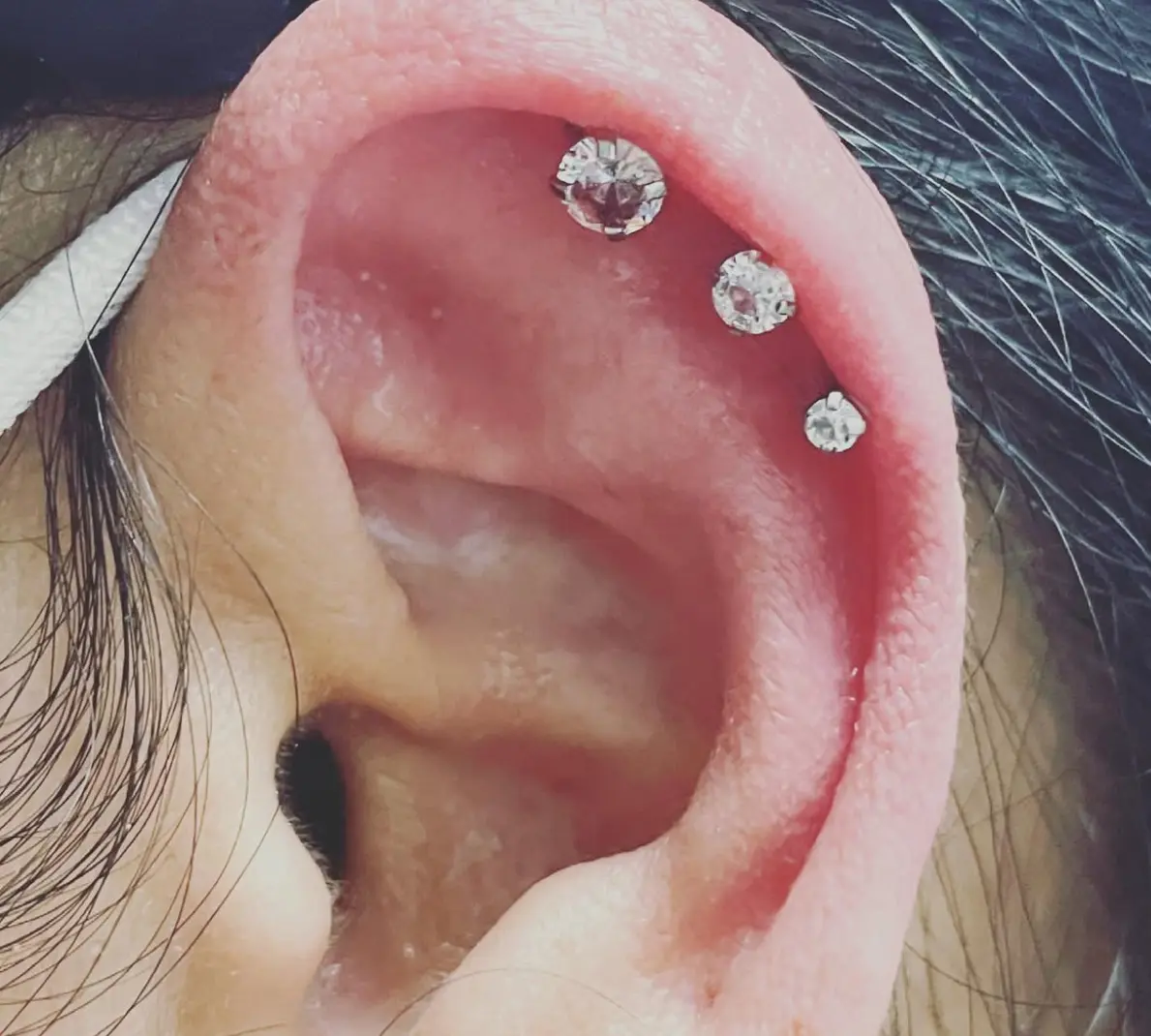 A close up of an ear with three piercings